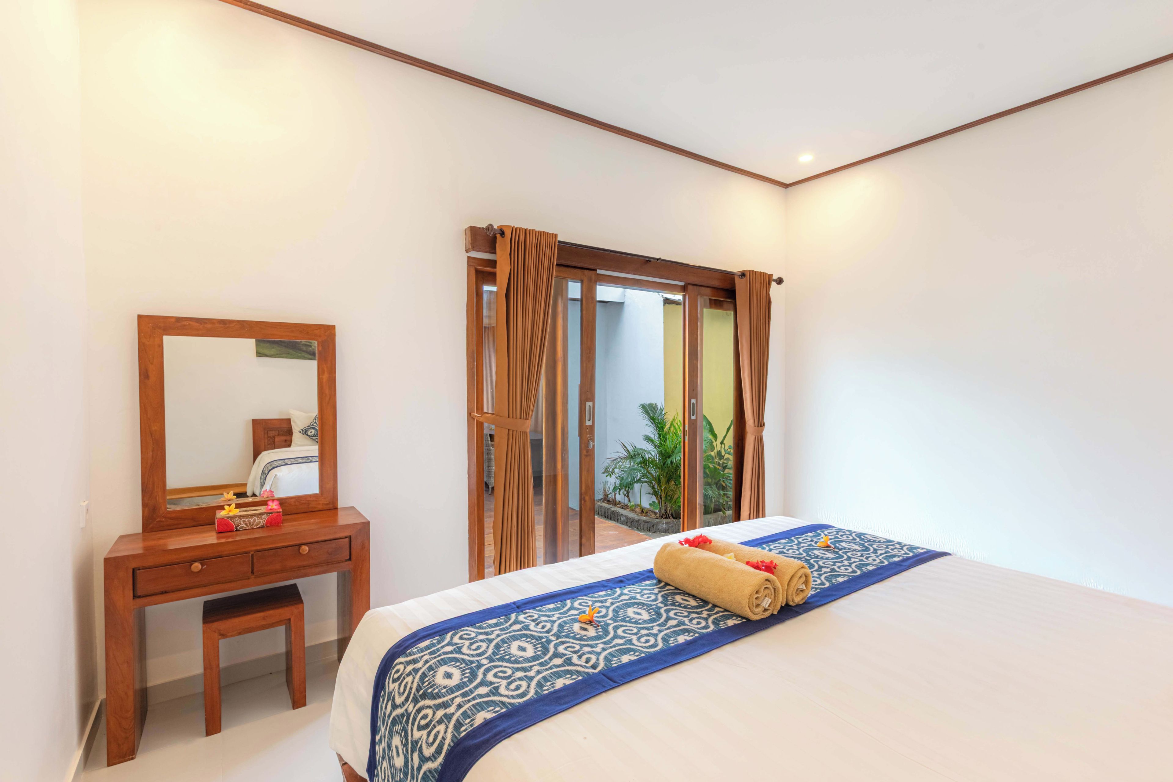 A hotel room with a bed, a wooden dresser, a mirror, and a sliding glass door to a balcony.