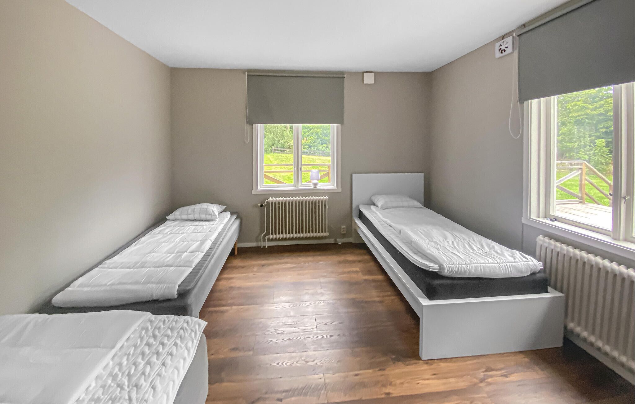 Ein Zimmer mit zwei Einzelbetten, einem Heizkörper, einem Fenster mit Blick ins Grüne und einem Deckenventilator.