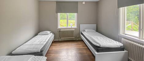A room with two single beds, a radiator, a window with a view of greenery, and a ceiling fan.