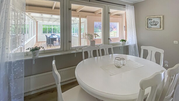 Ein Zimmer mit einem runden weißen Tisch und Stühlen, einem Fenster mit Blick auf eine Terrasse und einem gerahmten Bild an der Wand.