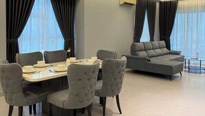 Una sala de estar moderna con comedor, mobiliario tapizado en gris y amplias ventanas con cortinas.