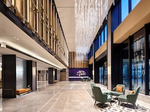 Un hall d’entrée spacieux avec un plafond haut, un coin salon avec des fauteuils et une table, ainsi qu’un comptoir d’accueil.