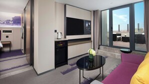 A modern hotel room with a large flat-screen TV, a small kitchenette, a sofa, and a balcony with a view of the city. - Hampton by Hilton Beijing Dahongmen (Beijing)