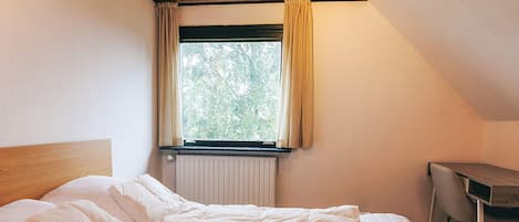 Une chambre à coucher avec un lit, une fenêtre avec des rideaux, un radiateur et un bureau avec une chaise.