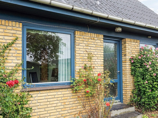 A brick house with a blue window frame, a door, and a small garden with roses.