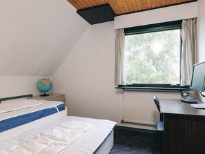 A room with a bed, a desk, a computer, a globe, and a window with curtains.