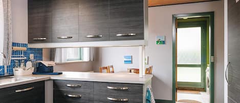 A modern kitchen with dark cabinetry, a white countertop, and a wooden ceiling.