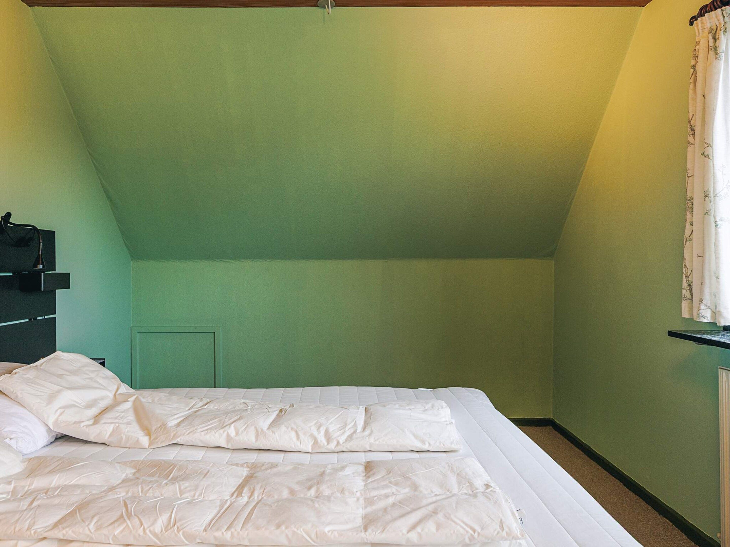 Un dormitorio con techo inclinado, una cama con ropa de cama blanca, una mesita de noche y una ventana con cortinas.