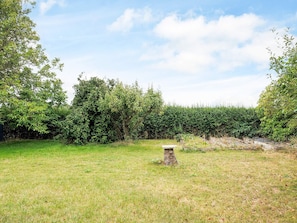 A grassy field with a stone structure, dense shrubbery, and a clear sky.