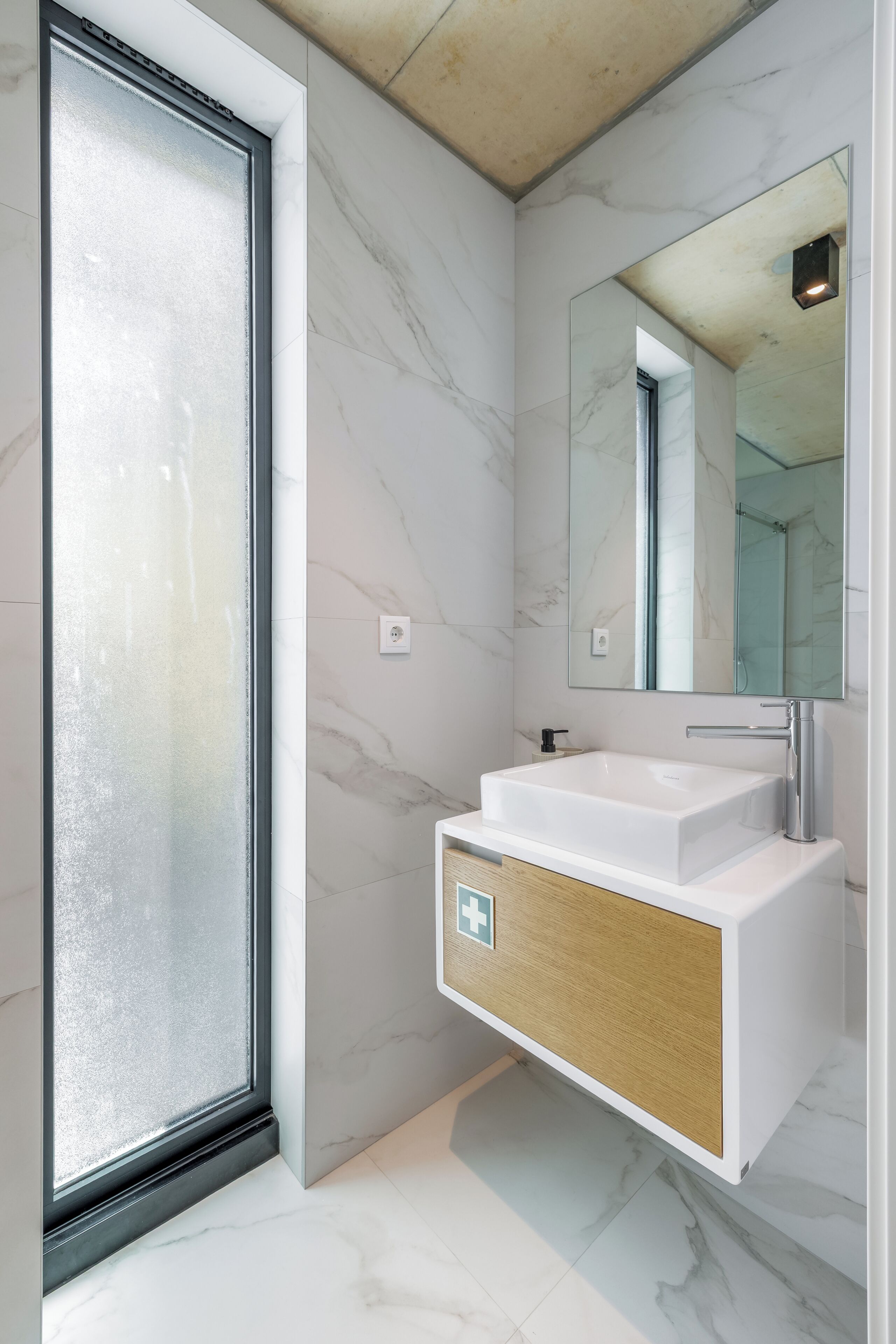 A modern bathroom with a large mirror, a white sink, and a frosted glass door.