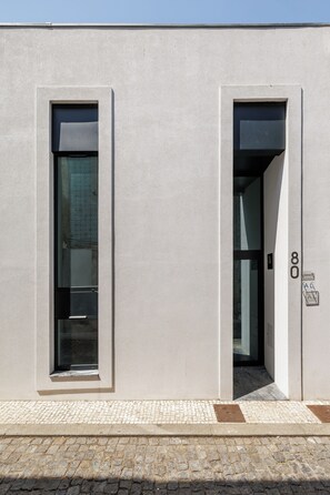 Fachada de edificio con dos puertas y un ventanal, con el número 80 visible en la puerta derecha.
