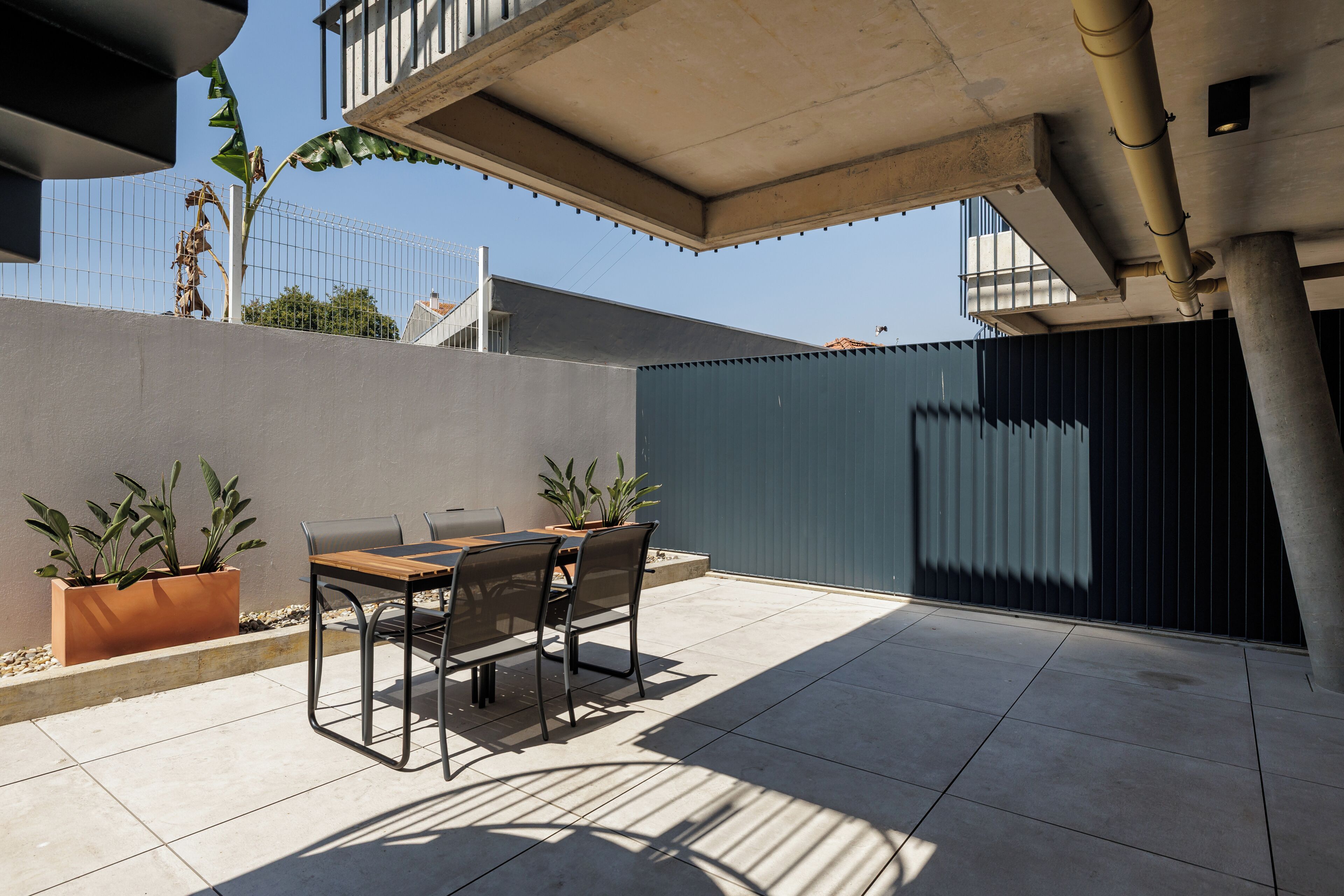 An outdoor patio with a table and chairs, surrounded by potted plants.