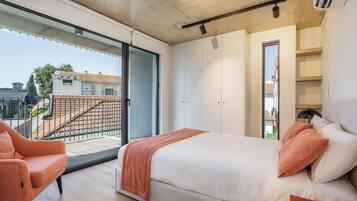 Un dormitorio moderno con una cama grande, una silla y un balcón con vistas a edificios.