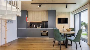 Una cocina moderna con armarios grises, horno empotrado y un comedor con mesa redonda y sillas verdes.