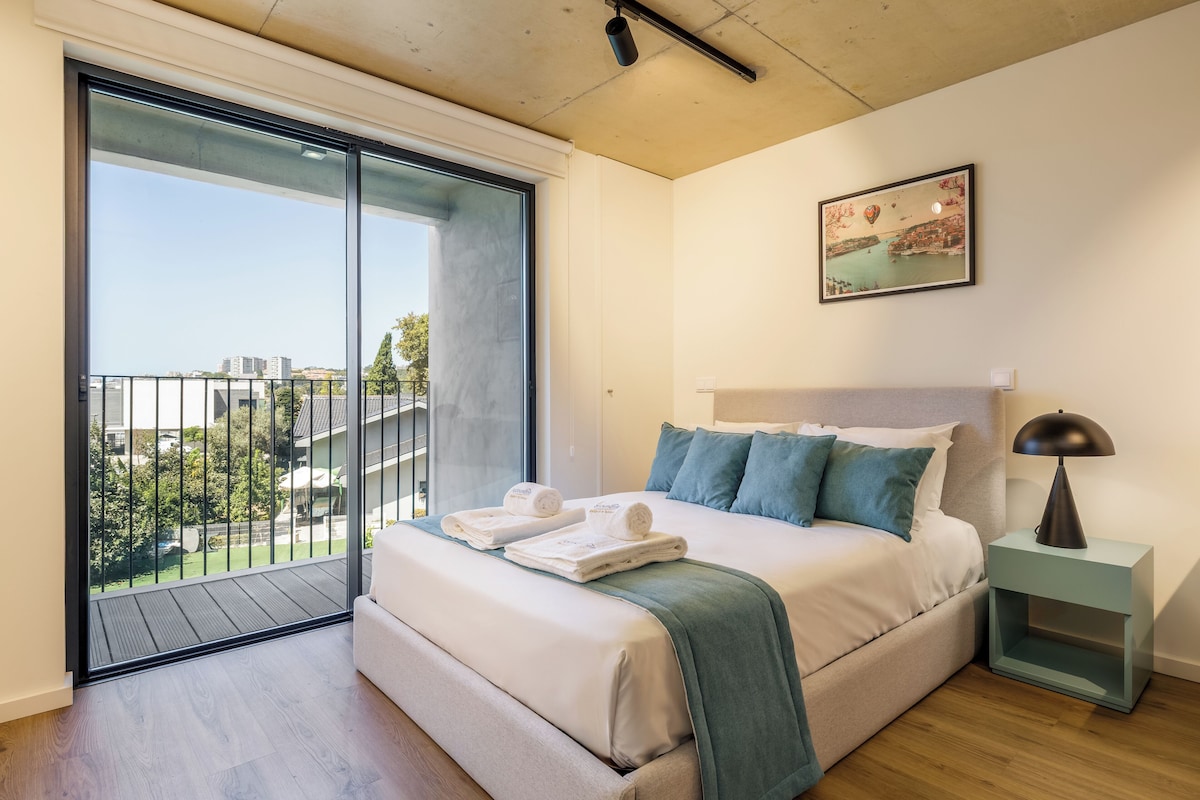 A modern bedroom with a large bed, a nightstand, a lamp, and a painting.
