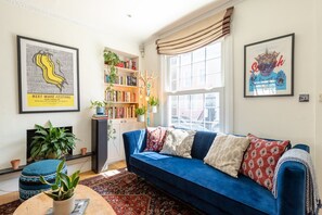 Uma sala de estar com um sofá azul, uma estante, uma lareira e obras de arte emolduradas nas paredes.