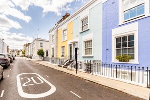 A street with a speed limit sign of 20, lined with colorful houses and parked cars. - Stylish Notting Hill Home with Patio (London)