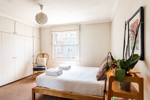 Quarto com cama, cadeira, janela e guarda-roupa.