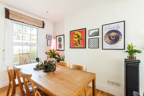A dining area with a wooden table and chairs, surrounded by framed artwork on the walls. - Stylish Notting Hill Home with Patio (London)