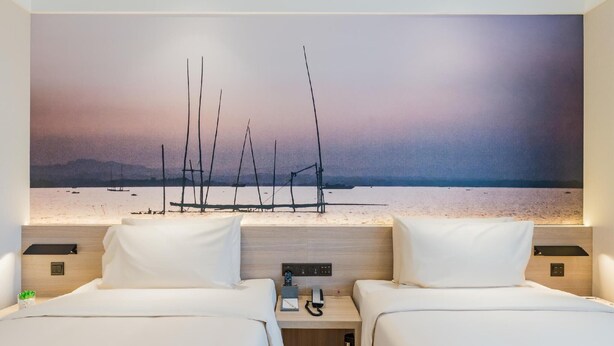 Een hotelkamer met twee bedden, een nachtkastje, een schilderij van zeilboten aan het strand en een houten hoofdbord.
