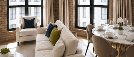 Una sala de estar moderna con sofá, mesa de comedor para cuatro comensales y ventanas grandes con cortinas.