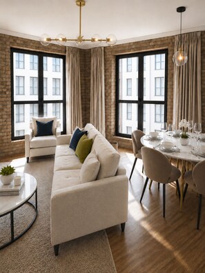 Ein modernes Wohnzimmer mit einer Couch, einem Esstisch für vier Personen und großen Fenstern mit Vorhängen.