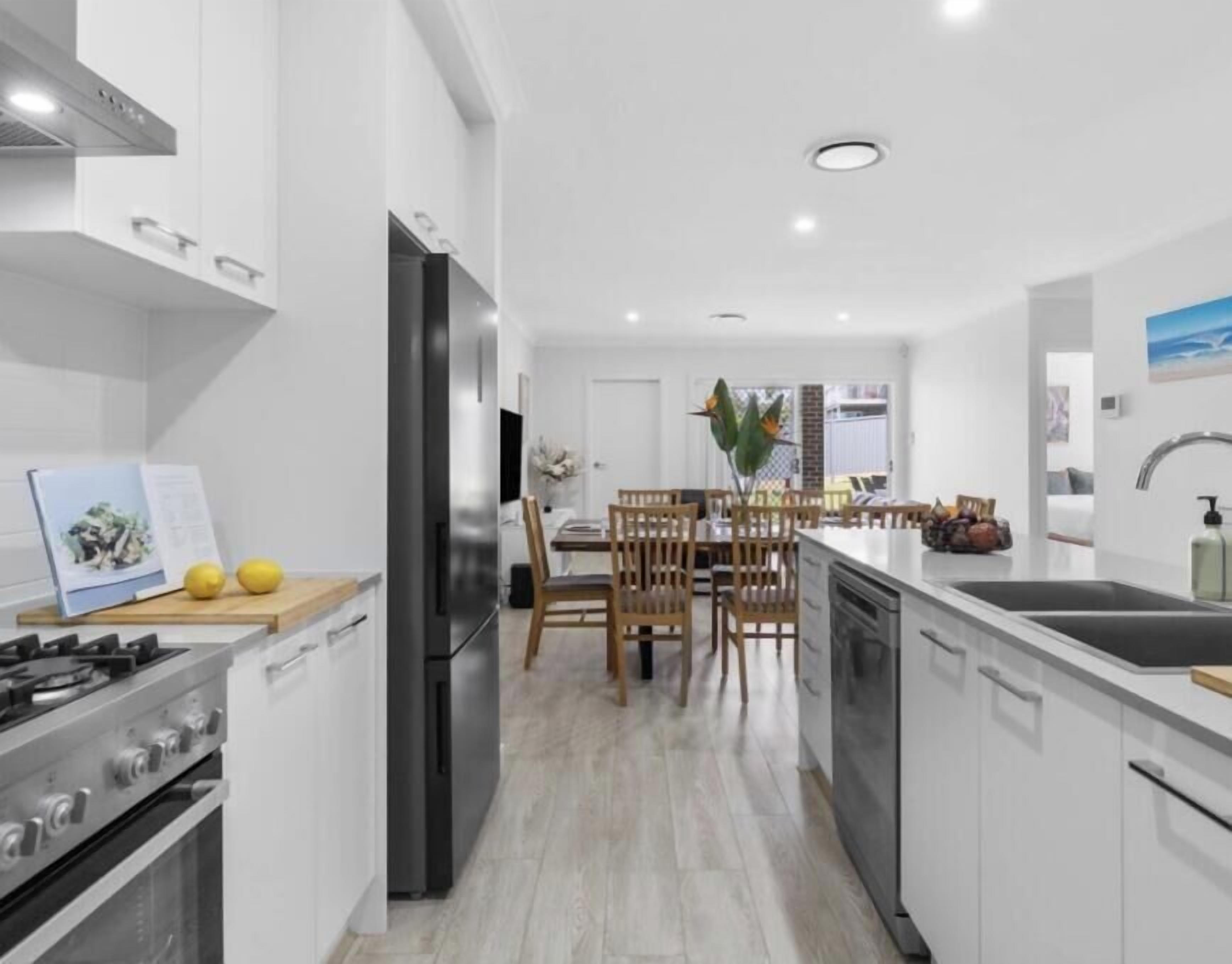Une cuisine moderne avec des meubles blancs, un îlot central et un coin repas doté de chaises en bois.