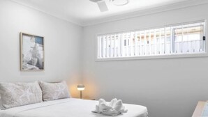 Ein Schlafzimmer mit einem Bett, einem Nachttisch, einer Lampe, einem Fenster mit Jalousien und einem Deckenventilator.