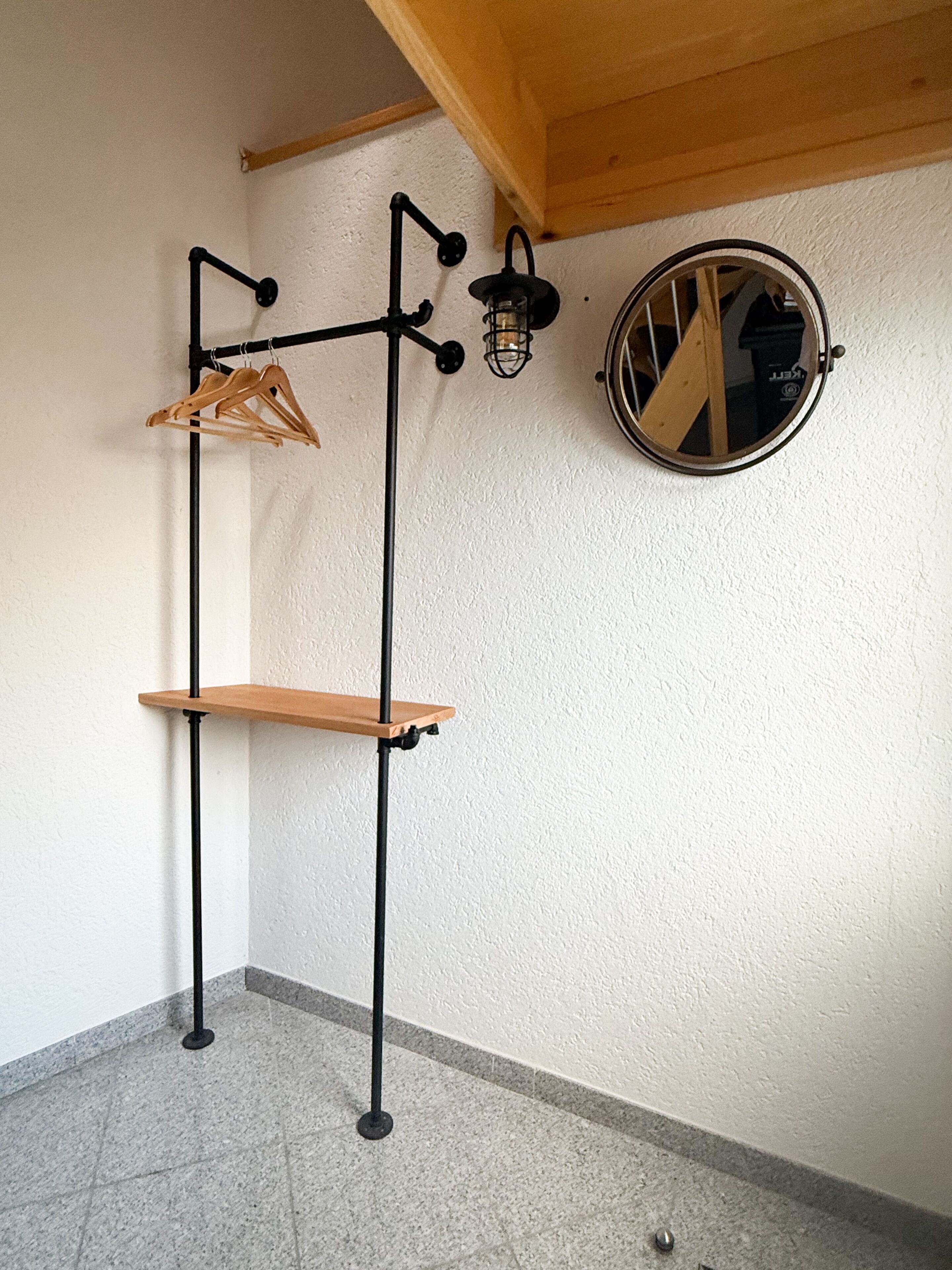 A corner of a room with a wooden shelf unit, a wall-mounted light fixture, and a round mirror.