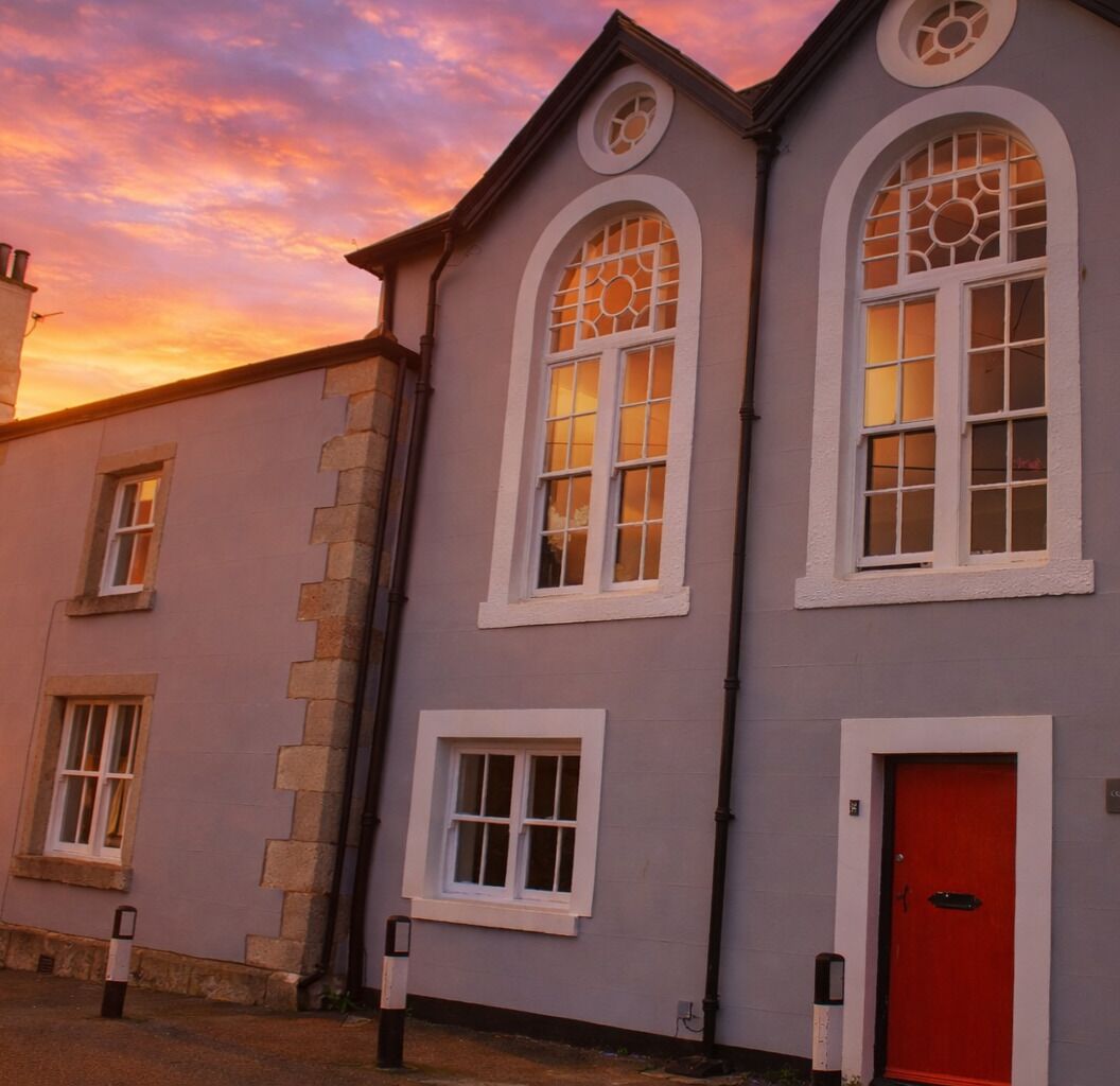 A building with a red door, white-framed windows, and a stone facade.