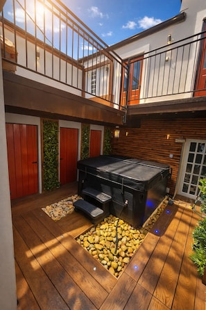 A multi-level outdoor space with a hot tub, wooden decking, and a balcony.