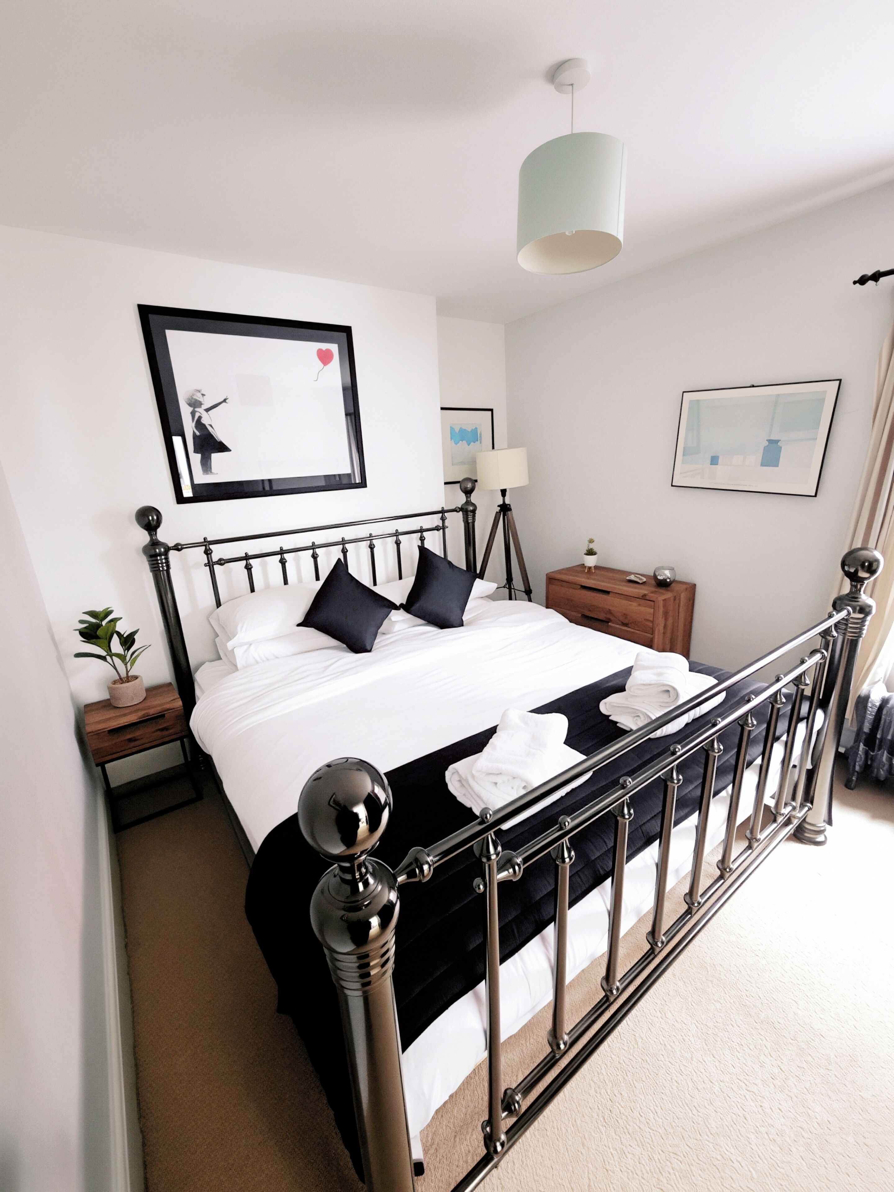 A neatly made bed with a black and white color scheme, a bedside table with a lamp, and a framed picture on the wall.