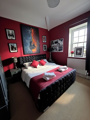 A bedroom with a large bed, red walls, and various framed pictures.