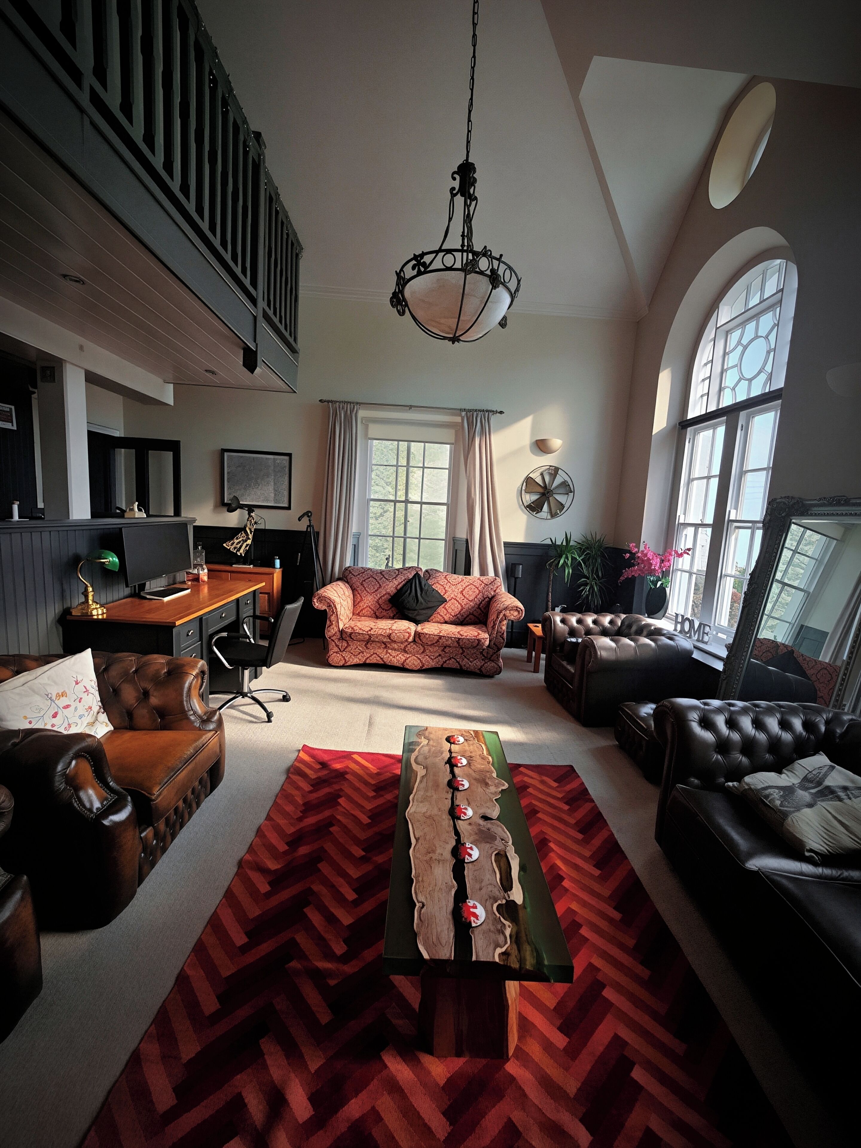 A spacious living room with a high ceiling, a large window, a fireplace, and a herringbone-patterned rug.