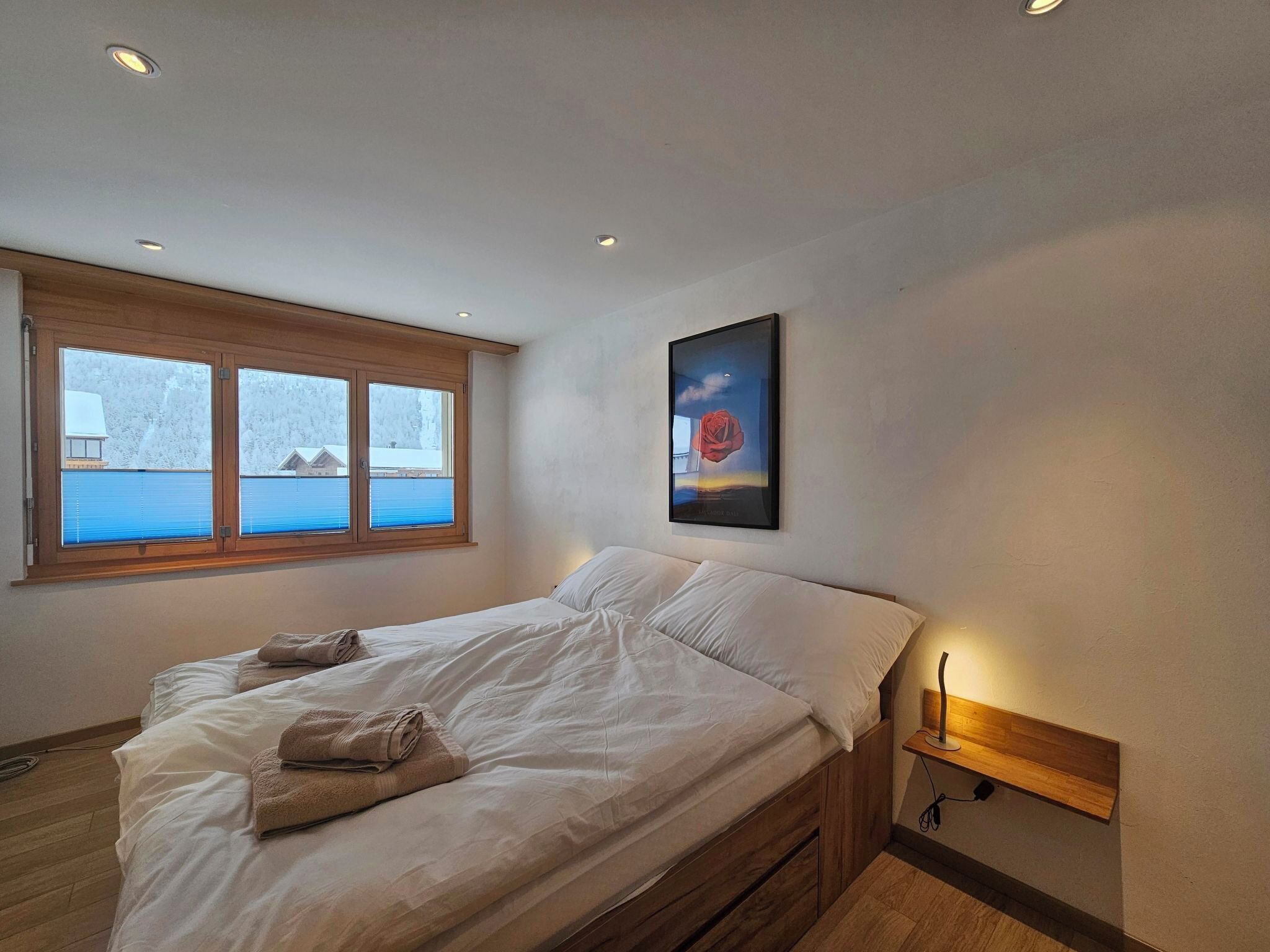Une chambre à coucher avec un lit, une fenêtre avec des stores, un tableau et une table de chevet.