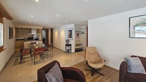 Ein geräumiger Wohnbereich mit einem Esstisch, zwei Sofas, einem Ledersessel und einer Küche im Hintergrund.