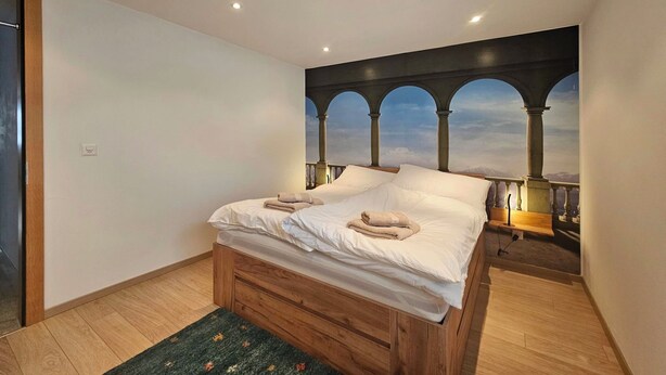 Ein Schlafzimmer mit einem Bett, Holzboden, einem Nachttisch und Wandgemälde mit Bögen.