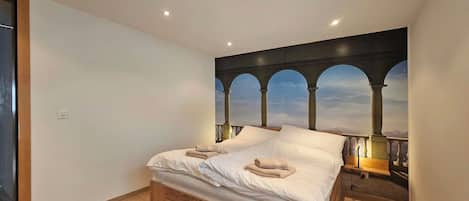 Un dormitorio con cama, piso de madera, mesita de noche y un mural en la pared con arcos.