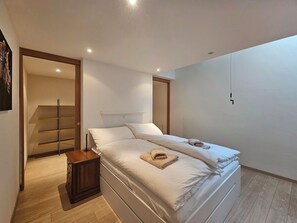 A bedroom with a bed, a bedside table, a wardrobe, and a door leading to another room. - Aramis EG by Interhome (Saas-Fee)