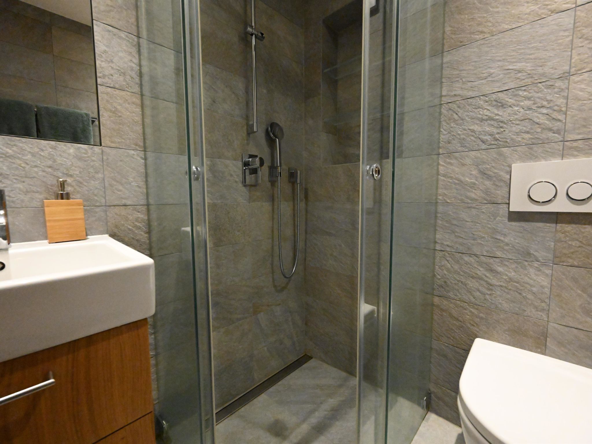 Un baño moderno con ducha envuelta en vidrio, un lavamanos blanco y un inodoro.