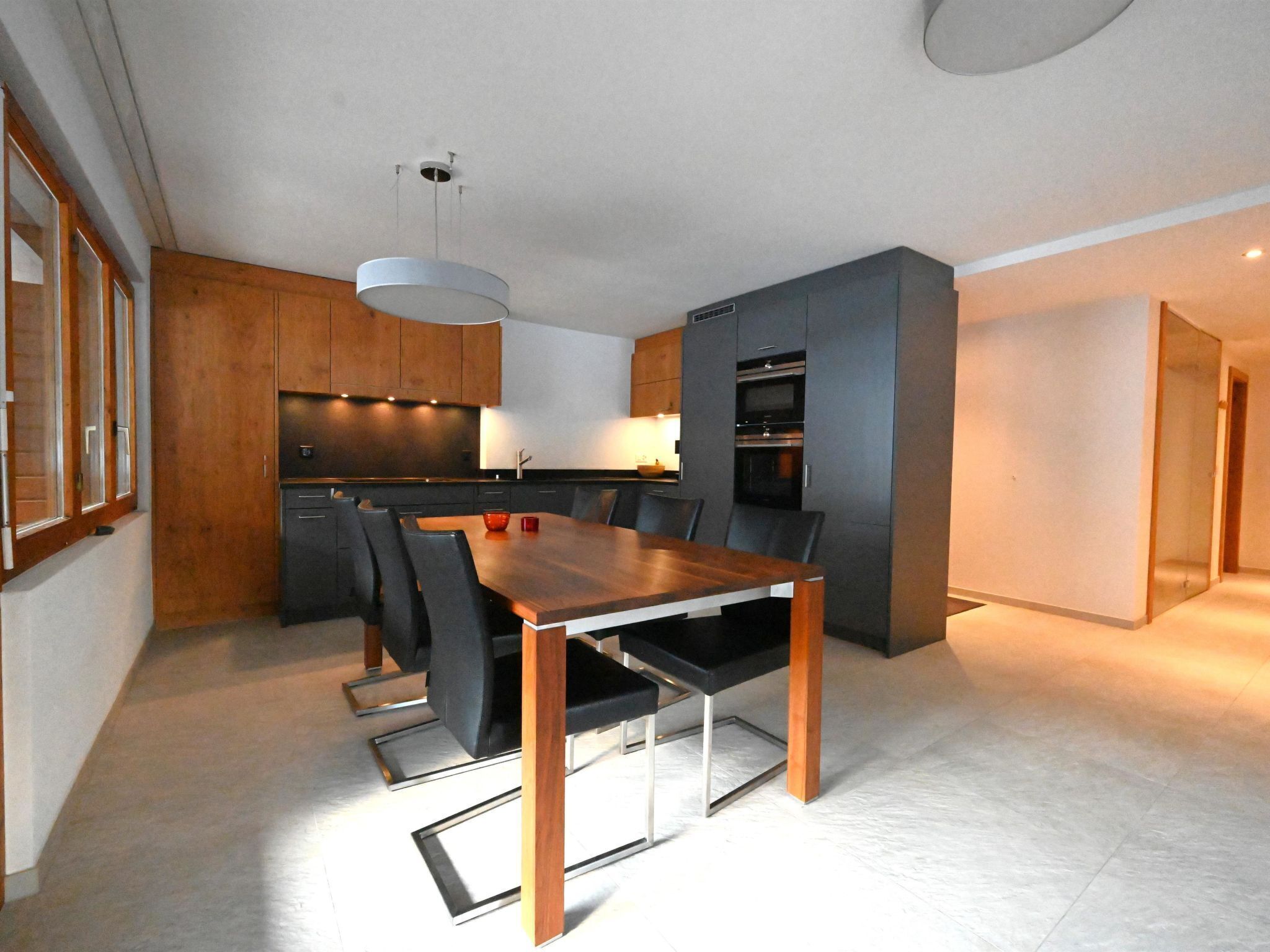 Una cocina moderna con armarios oscuros, una mesa de comedor de madera y sillas negras.