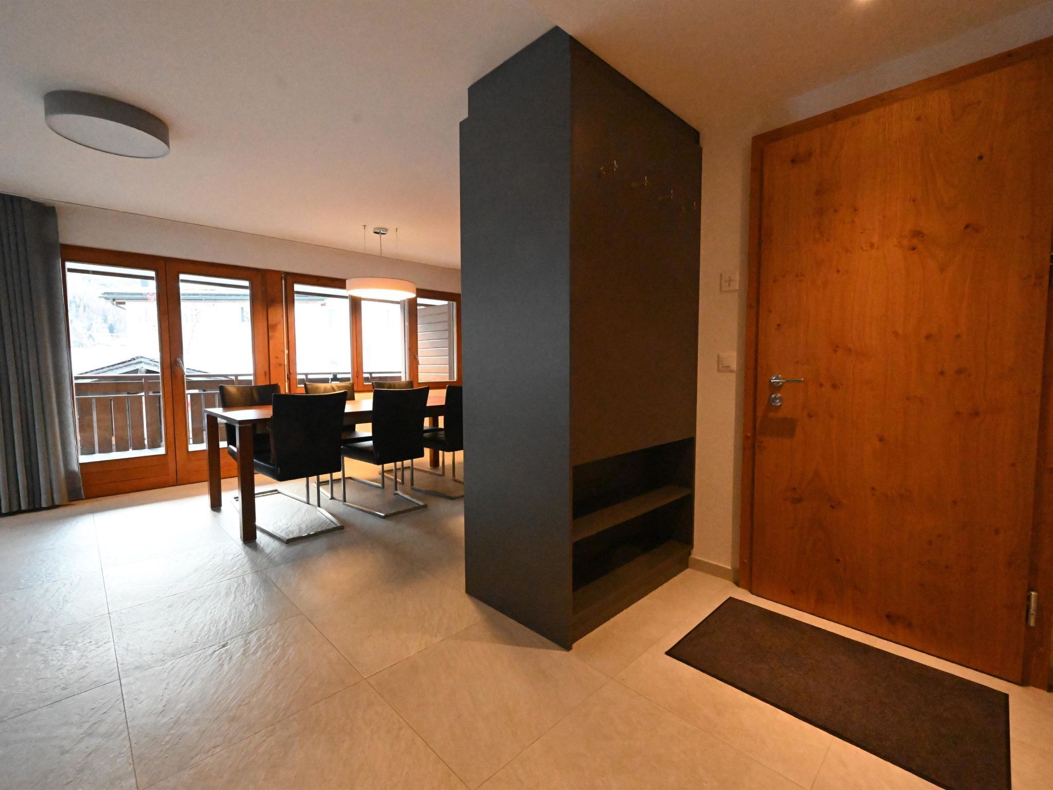 Een moderne woonkamer met een eethoek, grote ramen en een houten deur.