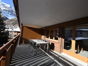 En balkong med ett bord och stolar, träväggar och utsikt över ett snötäckt berg.