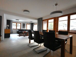 Ein geräumiger Wohnbereich mit Esstisch, Stühlen, einer Couch und großen Fenstern.