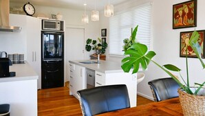 A modern kitchen with a central island, white cabinetry, a black refrigerator, and a dining area with a wooden table and chairs. - Pool & Spa - Havelock North (Havelock North)