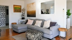 A modern living room with a grey sectional sofa, a patterned ottoman, and a large abstract painting. - Pool & Spa - Havelock North (Havelock North)