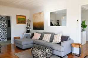 Ein modernes Wohnzimmer mit einem grauen Ecksofa, einem gemusterten Hocker und einem großen abstrakten Gemälde.