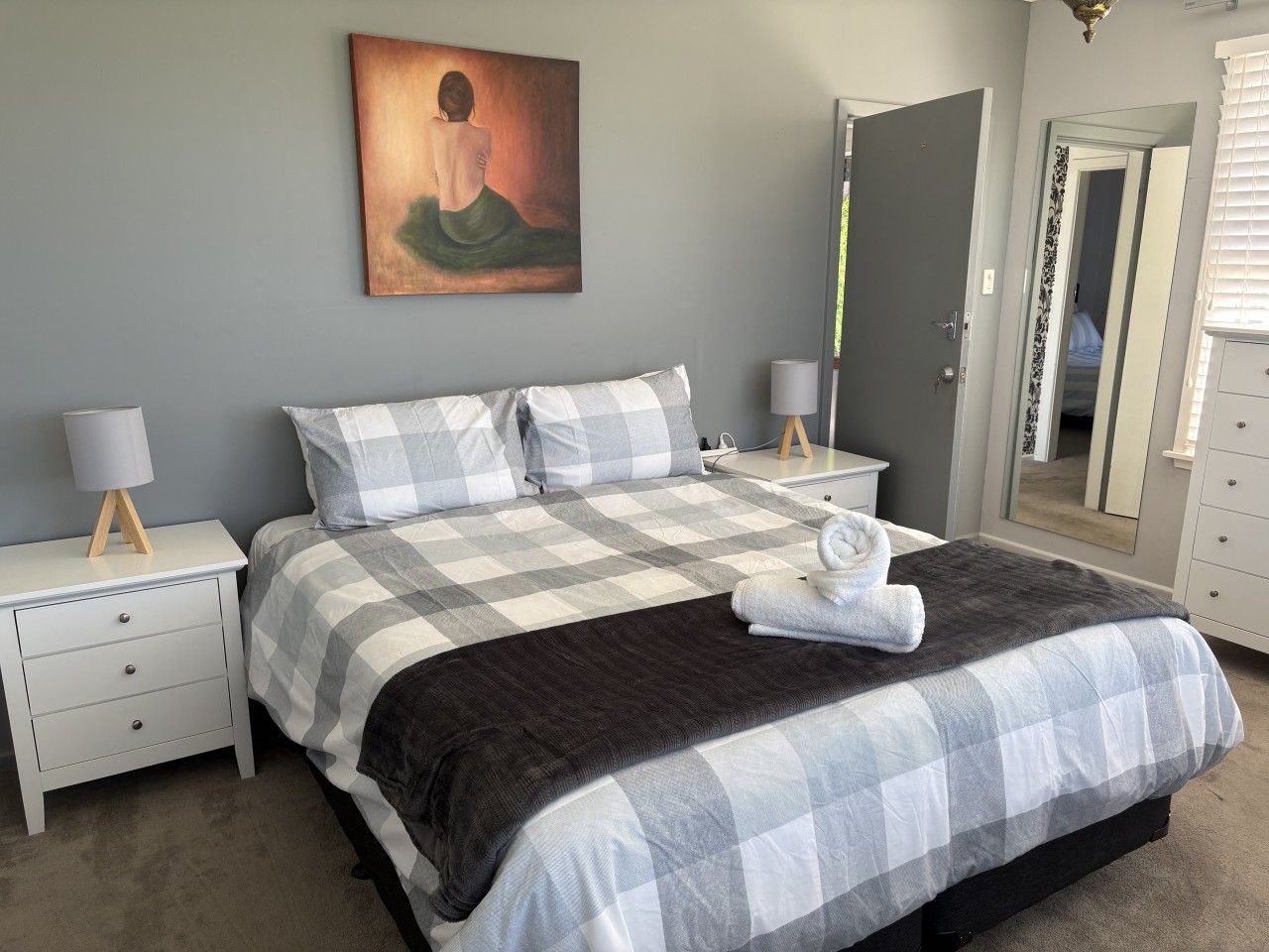 Un dormitorio con una cama, dos mesitas de noche, una mesilla auxiliar, un espejo y un cuadro en la pared.