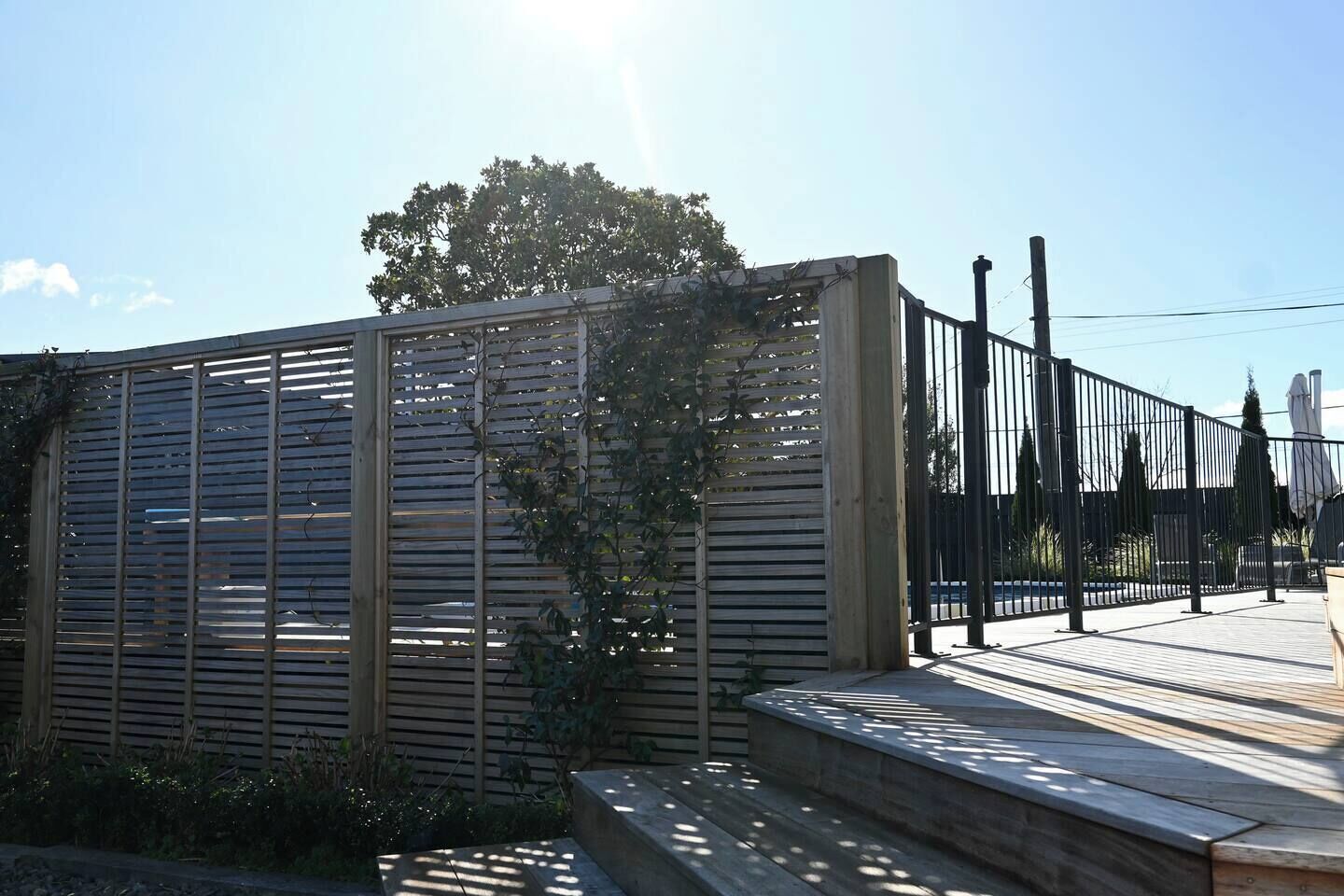 Un espacio exterior moderno con una valla de madera, un banco y un camino pavimentado.