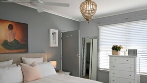 A bedroom with a bed, bedside table, lamp, dresser, and a painting on the wall. - Pool & Spa - Havelock North (Havelock North)